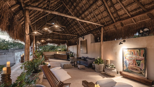 A cozy outdoor seating area with a thatched roof, cushioned seating, and potted plants. - Casa Kacaya (Espita)