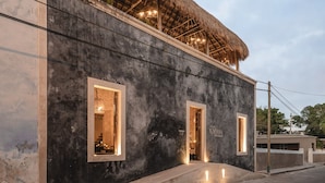 A building with a thatched roof and two illuminated windows. - Casa Kacaya (Espita)