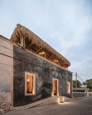 A building with a thatched roof and two illuminated windows. - Casa Kacaya (Espita)