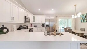 A modern kitchen with white cabinetry, a central island, and a dining area with a table and chairs. - Peaceful Retreat  3 Bedroom  10 min to WEC (Marion County)