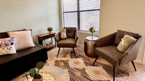 Ein Wohnzimmer mit einer Couch, zwei Sesseln, einem Couchtisch und einem Fenster mit Jalousien.