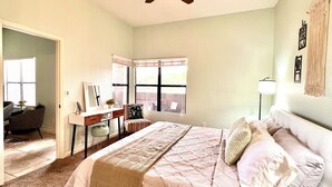 Ein Schlafzimmer mit Bett, Schreibtisch, Stuhl, Deckenventilator und Fenster.