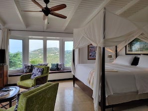A bedroom with a bed, a ceiling fan, a window with a view, and a green armchair.