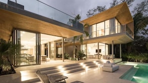 Una casa moderna con piscina, mobiliario exterior y grandes ventanales.
