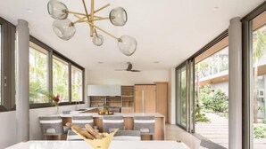 Una cocina moderna con una isla central, ventanas amplias y un comedor con mesa y sillas blancas.