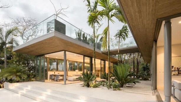Una casa moderna con un invernadero de cristal, mobiliario exterior y plantas tropicales.