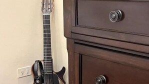 Eine dunkle Holzkommode mit drei Schubladen, eine Gitarre lehnt an der Wand.