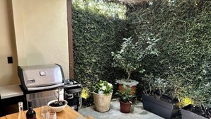 Eine Terrasse mit Grill, Esstisch und Blumentöpfen.