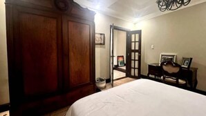 A bedroom with a large wooden wardrobe, a bed with white bedding, a chandelier, and a small table with a chair. - Elegant Escalante Home (San José)