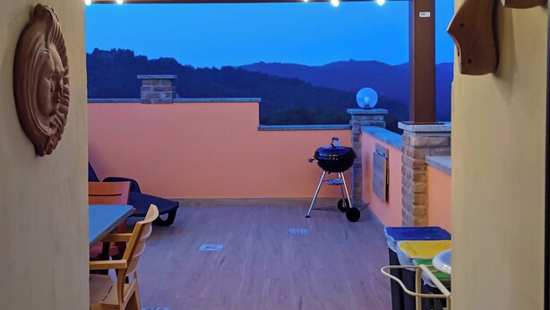 A covered outdoor patio with a view of the hills, a barbecue grill, and a dining area with chairs and tables. - A TERRACE IN THE GREEN apartment surrounded by nature, away from the hustle and bustle  (Lombardia)