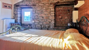 A cozy room with a stone wall, a wooden ceiling, a bed with a green metal frame, a window, and a radiator. - A TERRACE IN THE GREEN apartment surrounded by nature, away from the hustle and bustle  (Lombardia)