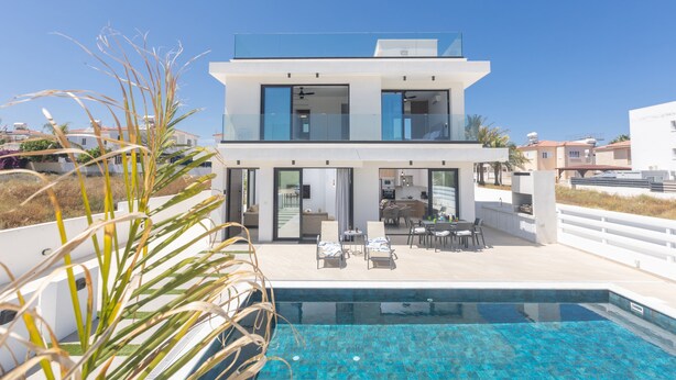 A modern two-story house with a swimming pool, outdoor seating area, and a view of the surrounding neighborhood.