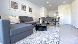 A modern living room with a grey sectional sofa, a black coffee table, and a dining area with a table and chairs. - Phaedrus Living: Limnaria Luxury Flat Vine 121 (Paphos)