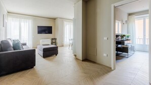 Ein geräumiges Wohnzimmer mit einer Couch, Hocker und einem an der Wand befestigten Fernseher.