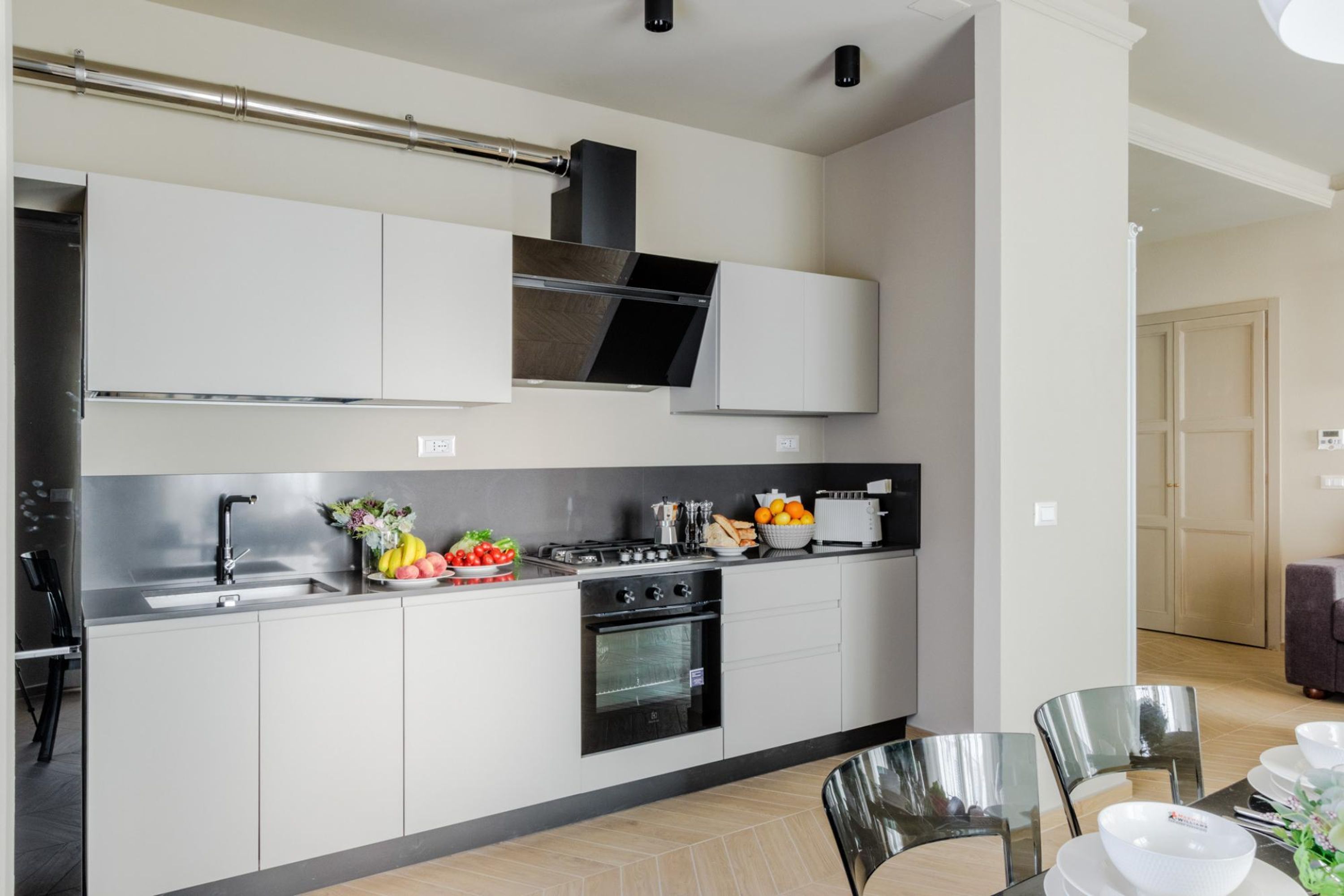 Una cocina moderna con armarios blancos, electrodomésticos de acero inoxidable y una zona de comedor con mesa y sillas.