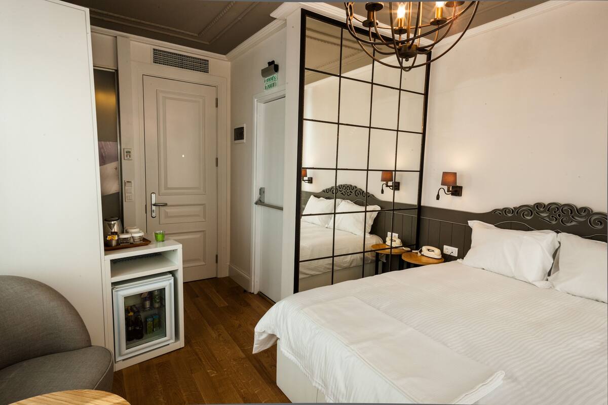 A hotel room with a bed, a small seating area, a mini-fridge, and a door leading to another room.