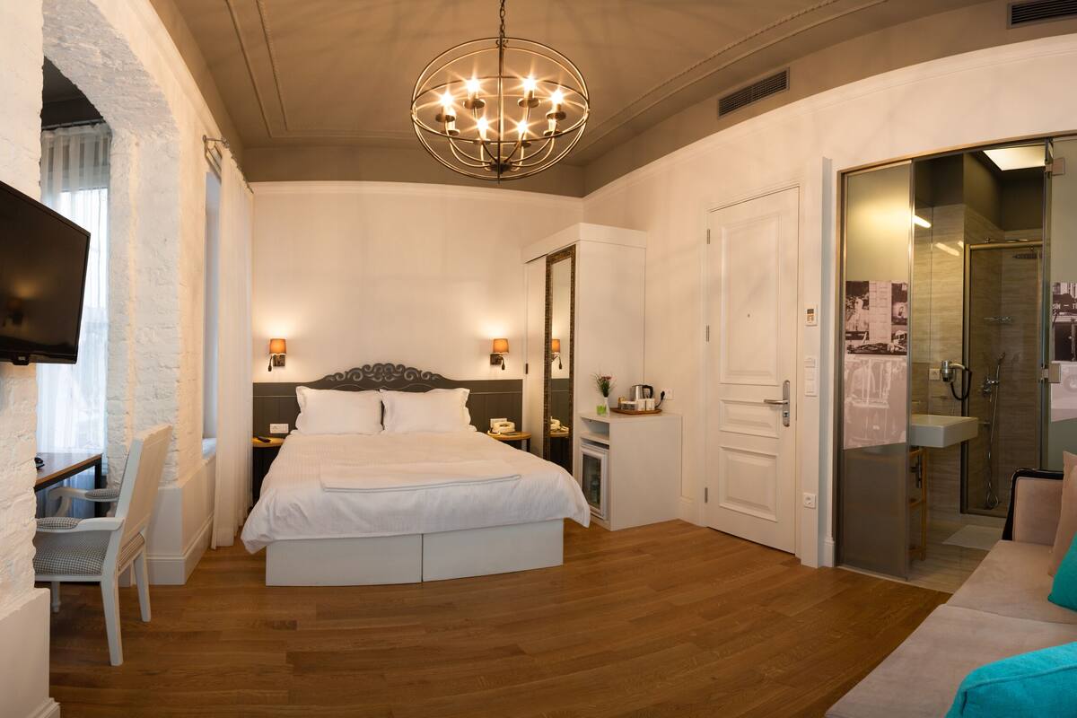 A modern bedroom with a large bed, bedside tables, a TV, and a glass-enclosed bathroom.