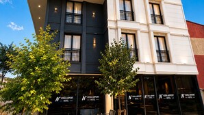 A multi-story hotel with a sign reading 'NORA AIRPORT HOTEL' and a visible entrance with seating outside. - Nora Airport Hotel Istanbul  (Arnavutköy)