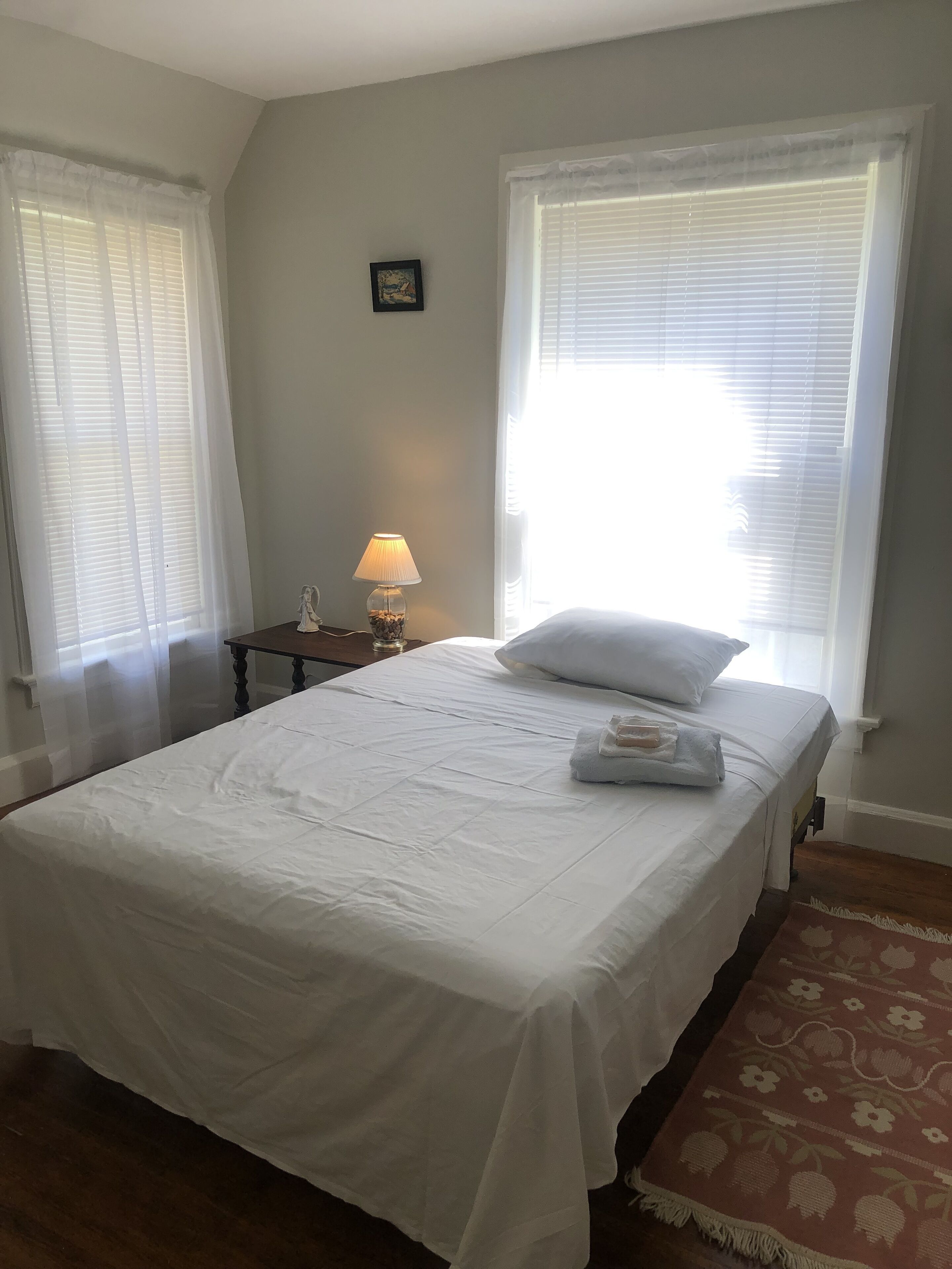 A neatly made bed with white linens, a bedside lamp, and a framed picture on the wall.
