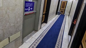 Un pasillo con paredes de mármol, alfombra azul y señales de salida de emergencia.