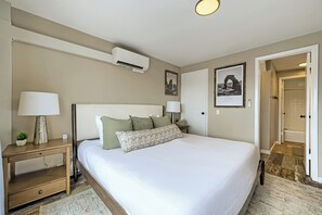 A hotel room with a bed, bedside tables, a lamp, an air conditioner, and a framed picture of a natural landmark. - The Ski Lift Loft 31 (Park City)