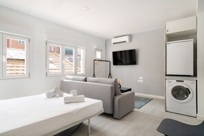 A modern, well-lit room with a sofa, a small table with towels, a washing machine, and a TV mounted on the wall. - Madrid Río Suites · parque, metro y parking gratis (Madrid)