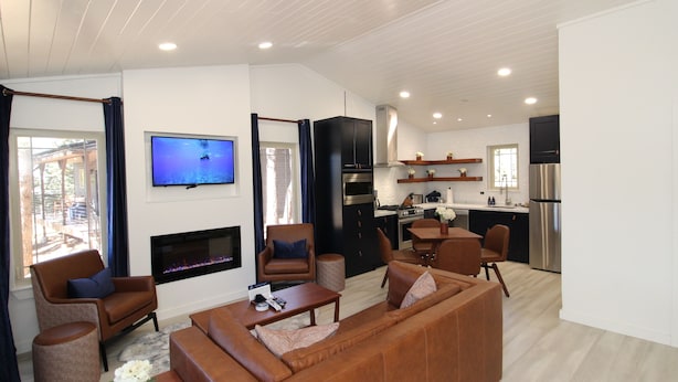 A modern living room with a sofa, armchairs, and a flat-screen TV. A kitchen is visible in the background with a refrigerator and stove. - Aspen Springs Angel fire (Angel Fire)