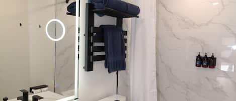 A modern bathroom with a white marble sink, a toilet, and a bathtub with a shower curtain.