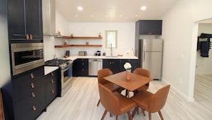 A modern kitchen with dark cabinetry, stainless steel appliances, and a wooden dining table with chairs. - Aspen Springs Angel fire (Angel Fire)
