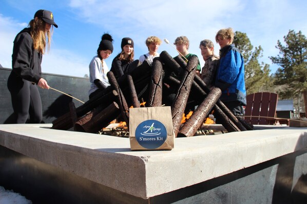 A group of people gathered around a grill with a bag labeled "S'mores Kit" in the foreground. - Aspen Springs Angel fire (Angel Fire)