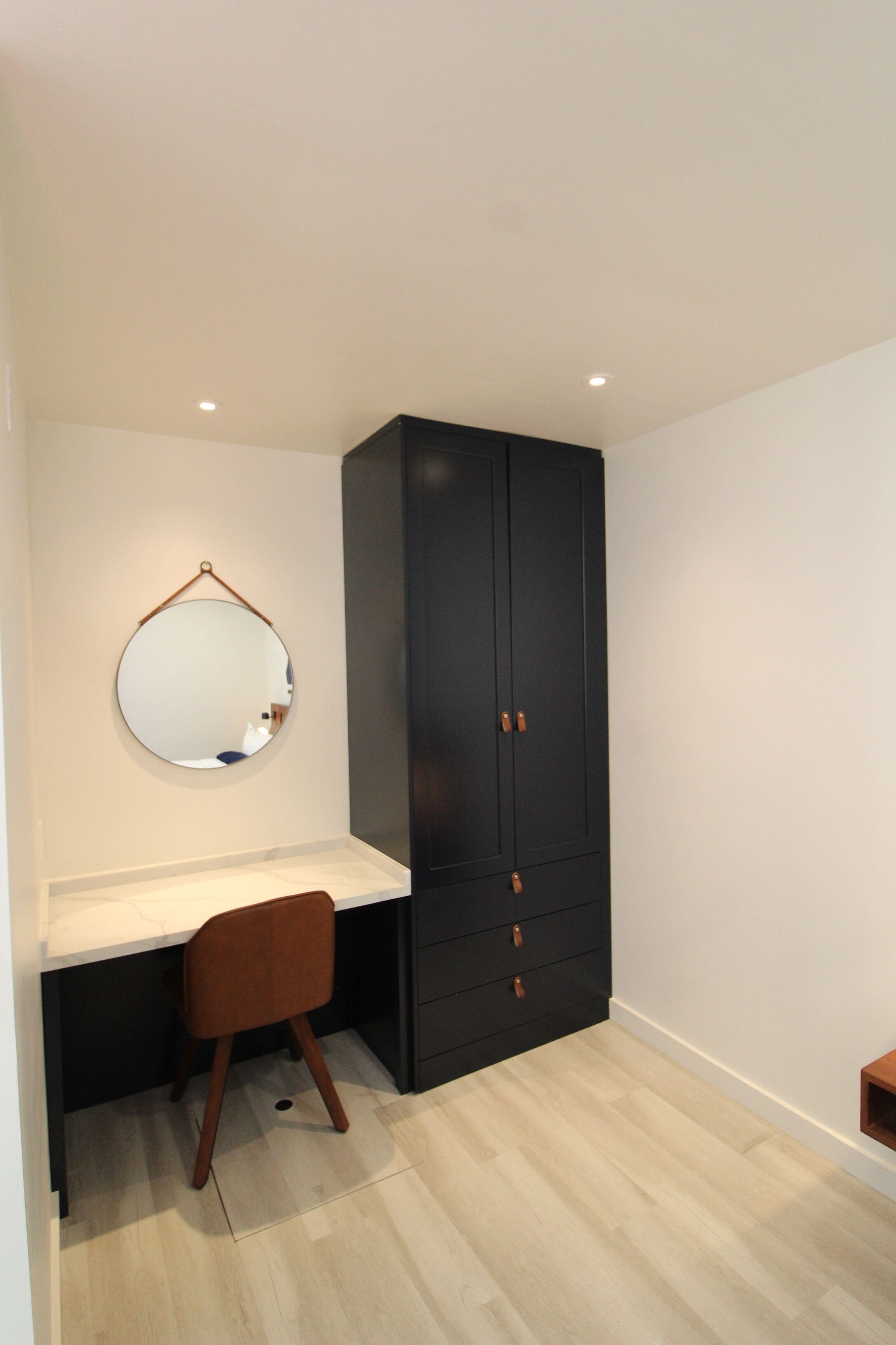 Une pièce avec une armoire en bois sombre, un miroir rond accroché au mur et une petite chaise en bois.