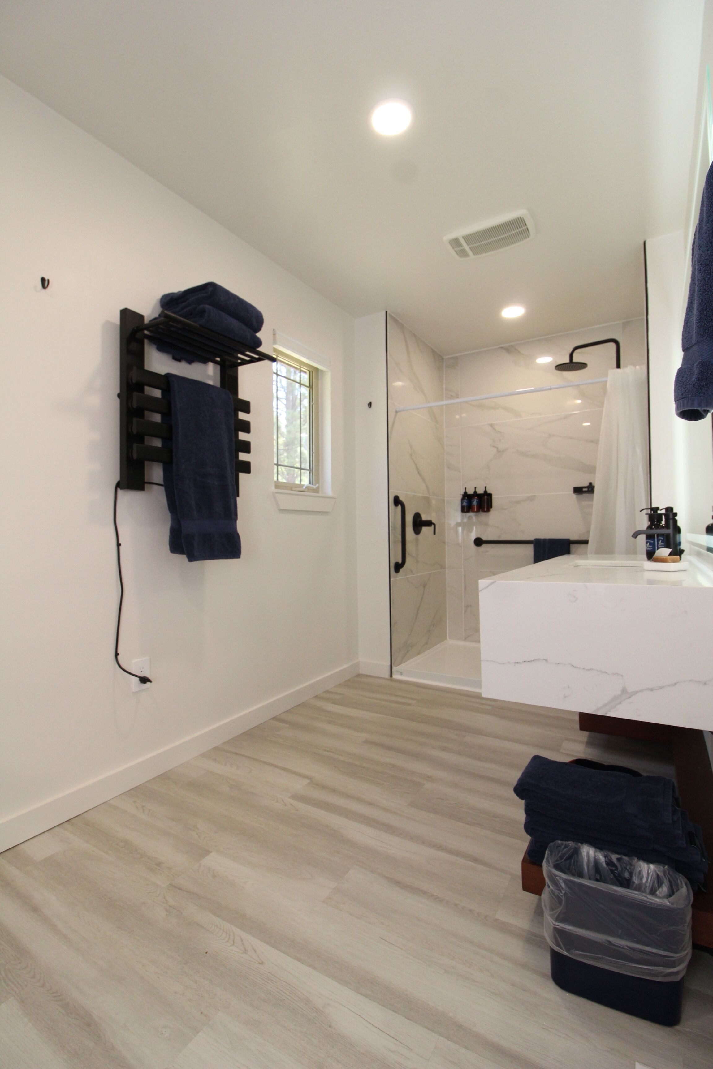 A modern bathroom with a glass shower enclosure, a white marble sink, and a towel rack with folded towels.