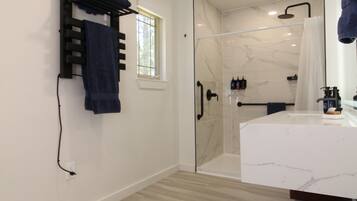 A modern bathroom with a glass shower enclosure, a white marble sink, and a towel rack with folded towels.