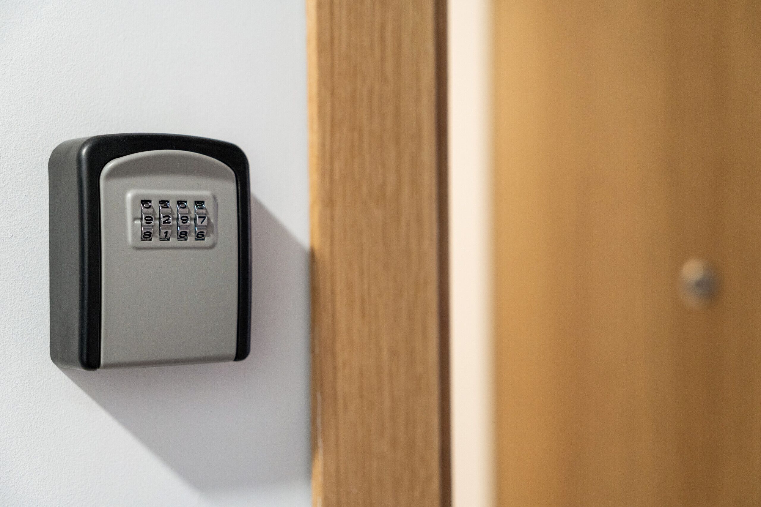 A keypad lock on a wall, next to a wooden door.
