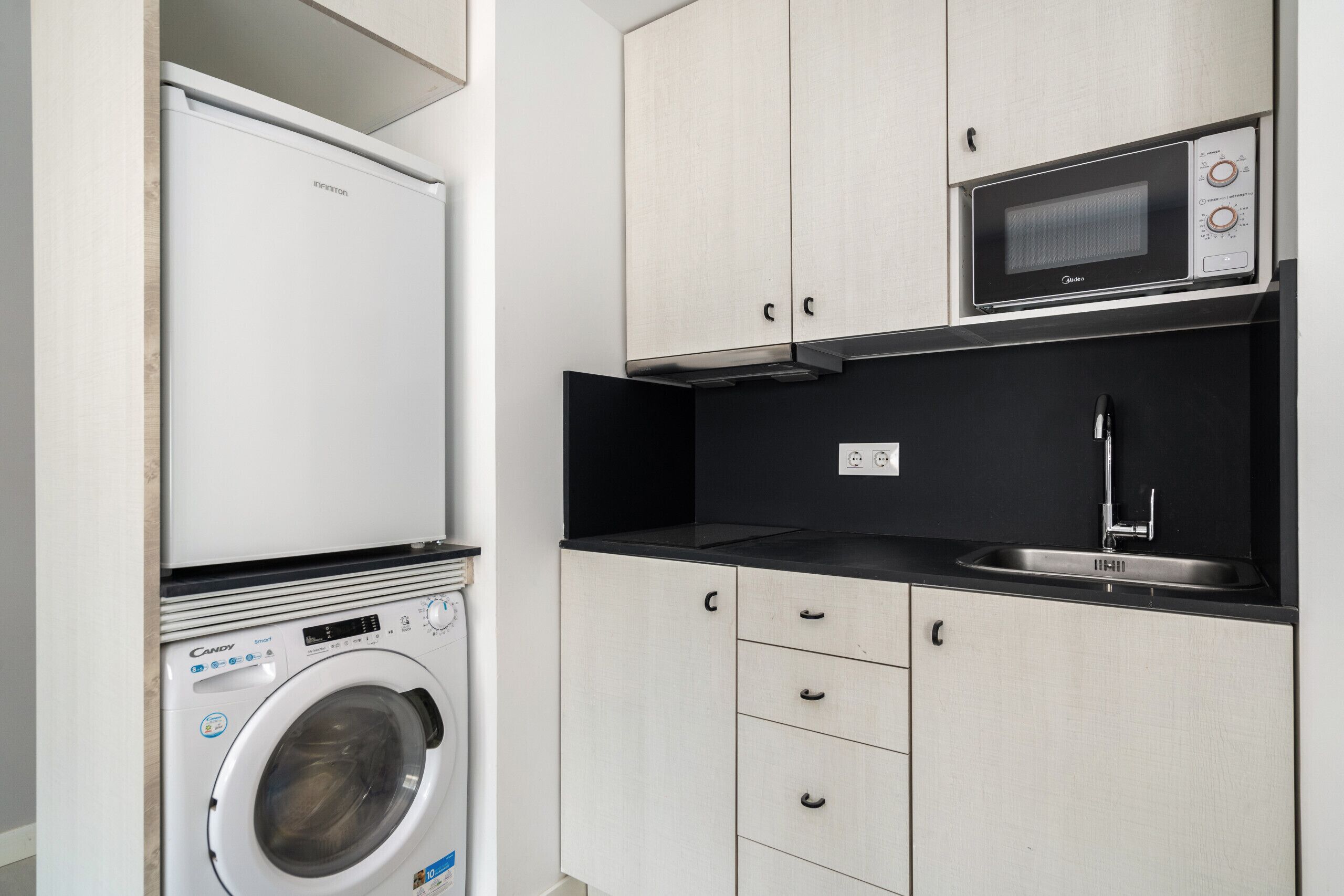 Une cuisine compacte équipée d’un lave-linge, d’un four à micro-ondes et d’un évier.