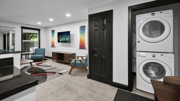 A modern laundry room with two stacked washing machines, a black door, and a colorful abstract painting on the wall. - Escape to This Gorgeous new Wilton Manors Villa (Wilton Manors)