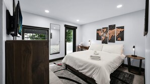 A modern hotel room with a large bed, a desk, a chair, a TV, and a world map on the wall. - Escape to This Gorgeous new Wilton Manors Villa (Wilton Manors)