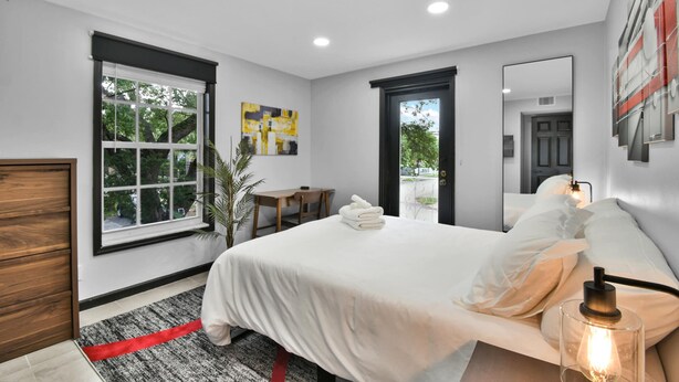 Een moderne slaapkamer met een groot bed, een bureau, een stoel en een raam met uitzicht op bomen.