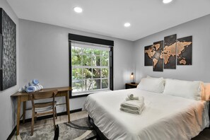 Ein modernes Hotelzimmer mit einem großen Bett, einem Schreibtisch mit Stuhl, einem Fenster mit Blick auf Grünflächen und Wandkunst, darunter eine Weltkarte.