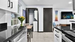 A modern kitchen with a central island, a dining area, and a view of the cityscape through the window.