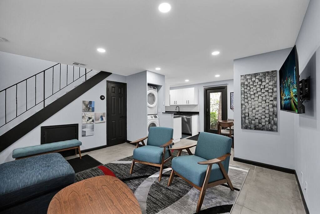 A modern living room with a staircase, a kitchen, and a dining area.