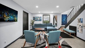 A modern living room with a sectional sofa, two armchairs, a coffee table, and a staircase with a black railing.