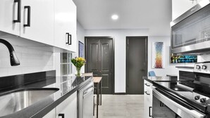 A modern kitchen with white cabinetry, a black countertop, stainless steel appliances, and a small dining area with a table and chairs.