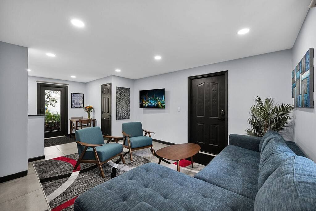 Ein modernes Wohnzimmer mit einer Couch, zwei Sesseln, einem Couchtisch und einem Fernseher an der Wand.
