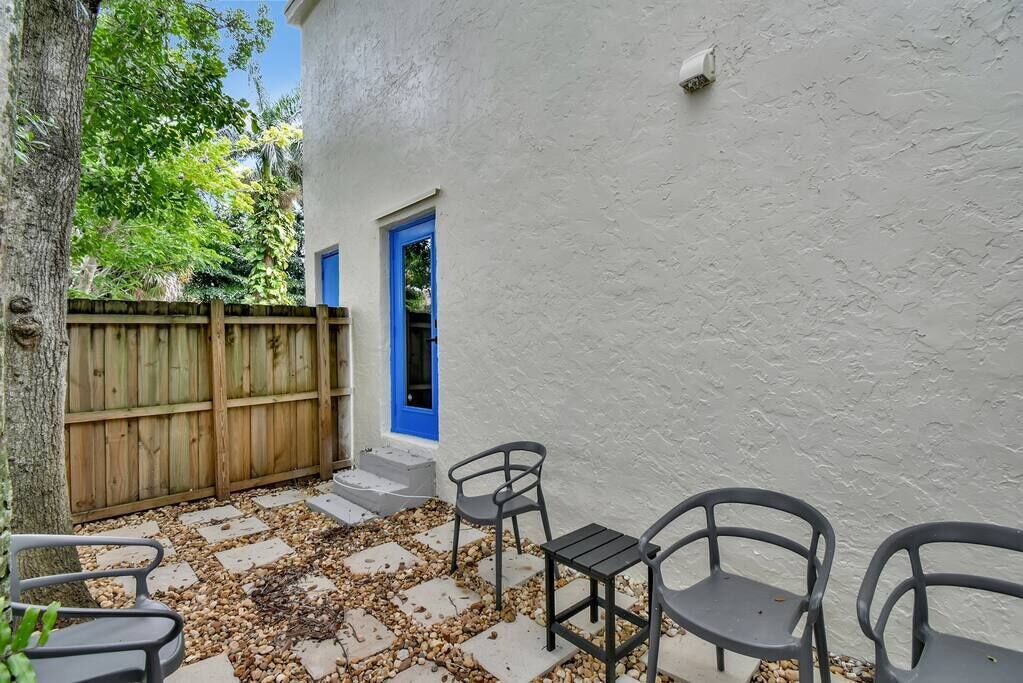 Une terrasse avec un mur blanc, une porte bleue et une clôture en bois.