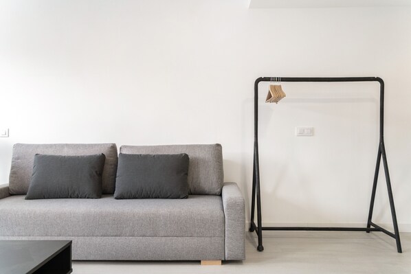 A grey sofa with two cushions, a black metal stand, and a white wall.
