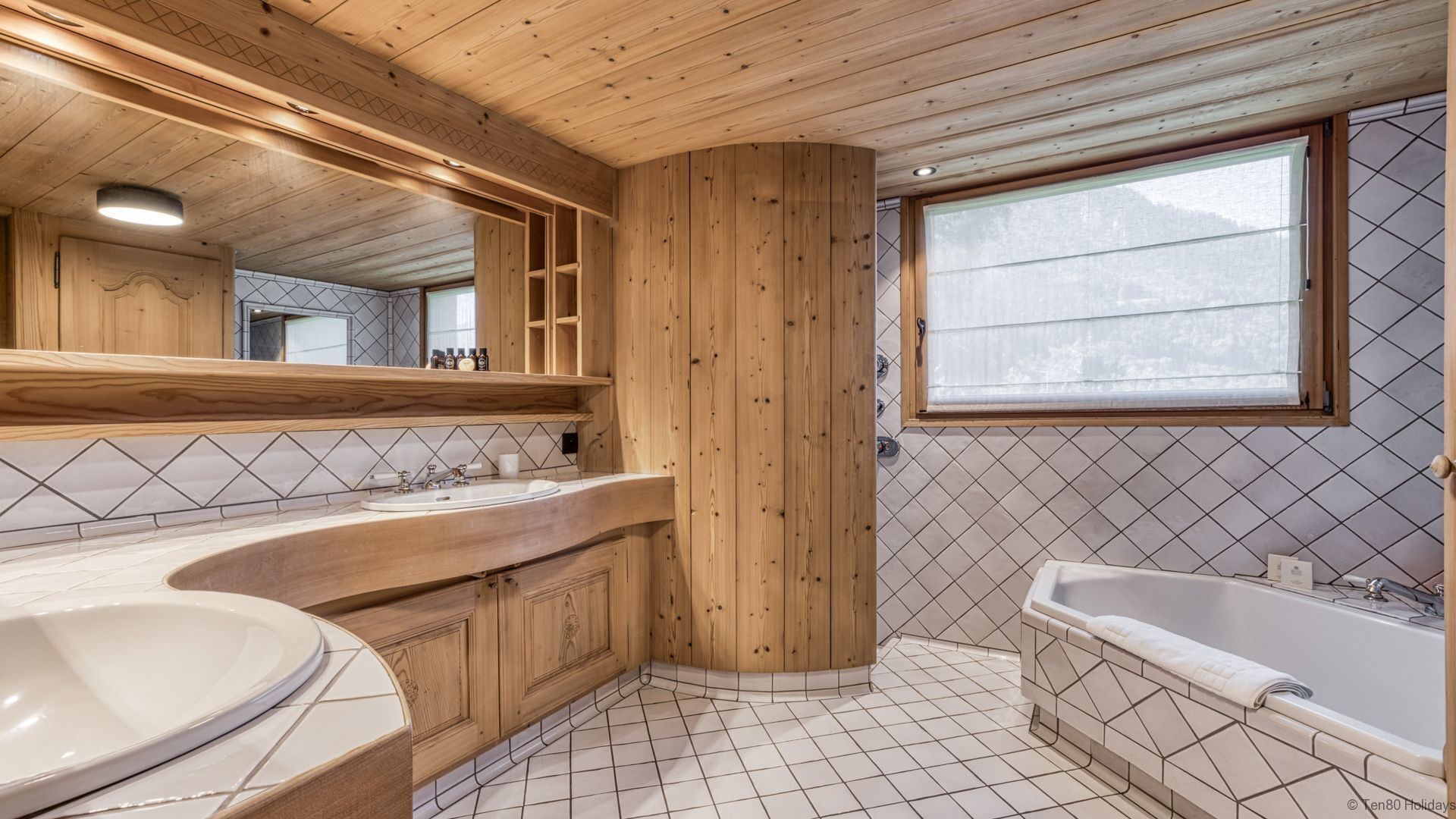 Een badkamer met houten kastjes, een grote spiegel, een wastafel, een badkuip en een raam met uitzicht.
