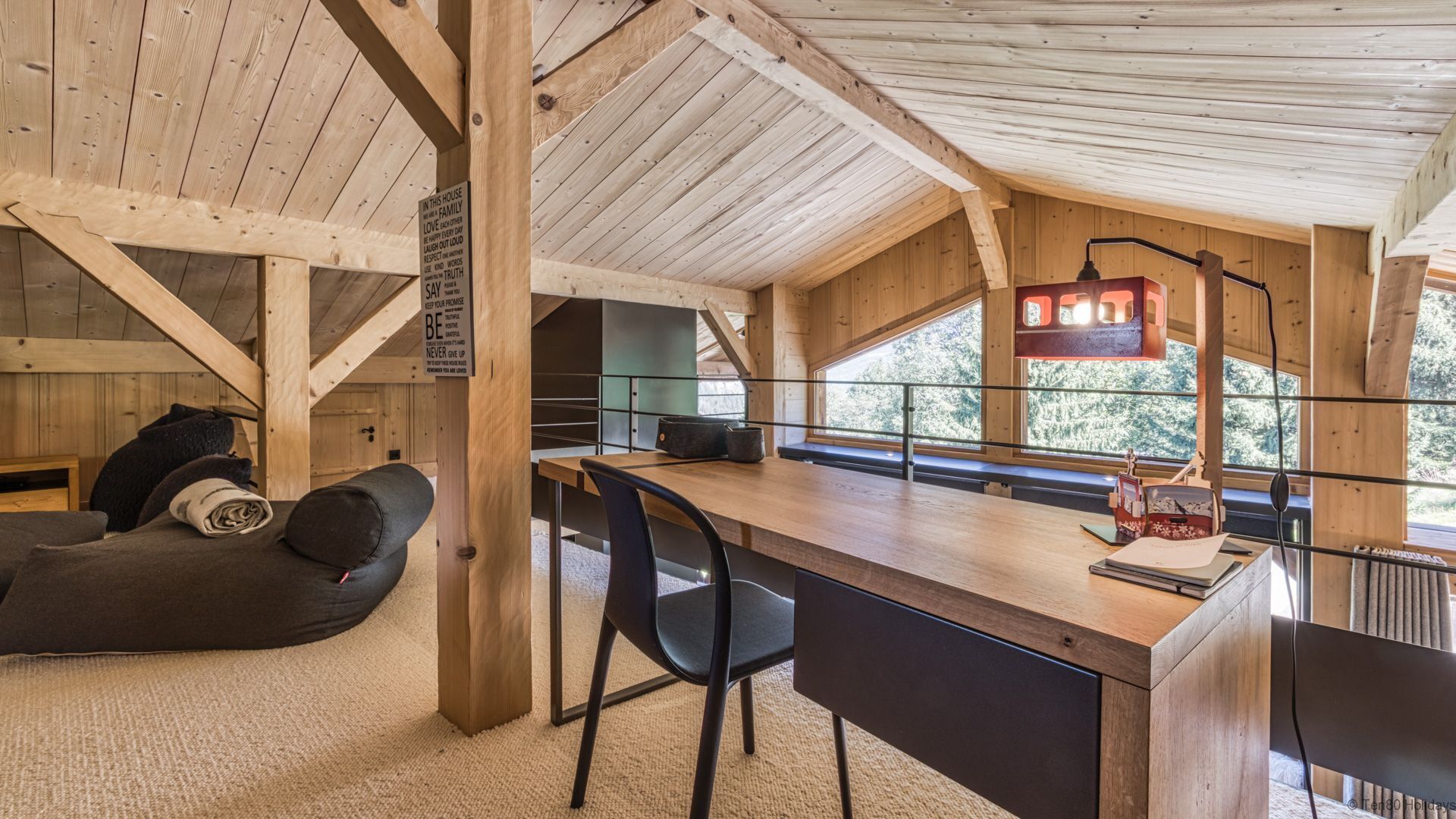 Ein gemütliches Blockhaus-Interieur mit Holzbalkendecke, einem Essbereich mit Tisch und Stühlen, einer Couch und Blick ins Freie durch große Fenster.