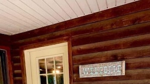 A wooden cabin with a white door, a welcome sign, and a doormat.