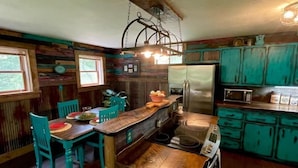 A rustic kitchen with wooden cabinets, a central island, and a hanging light fixture.